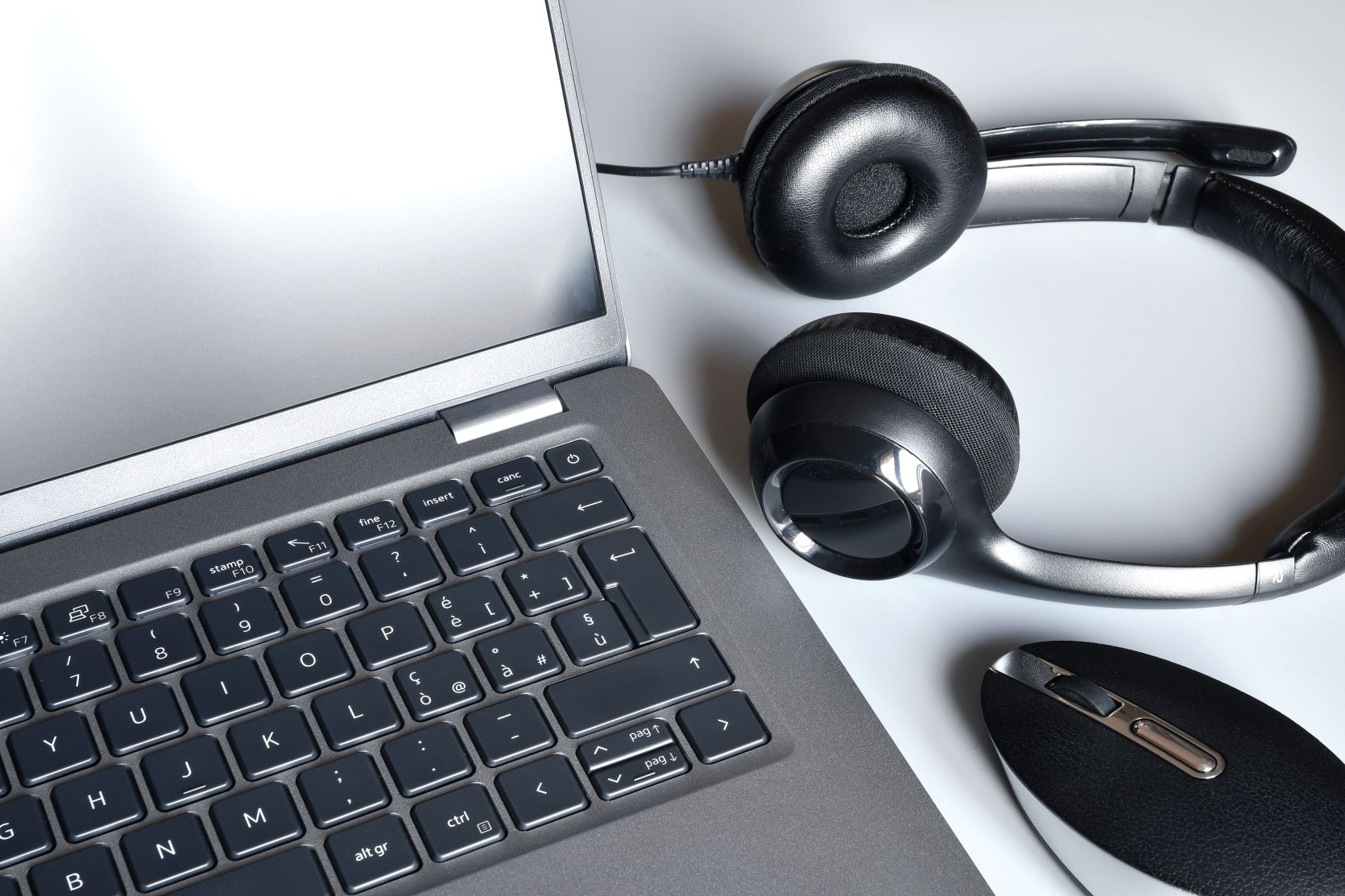 Work space with laptop, headphones and computer mouse on white office desk.
